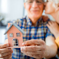 New house concept, happy senior couple holding small home model